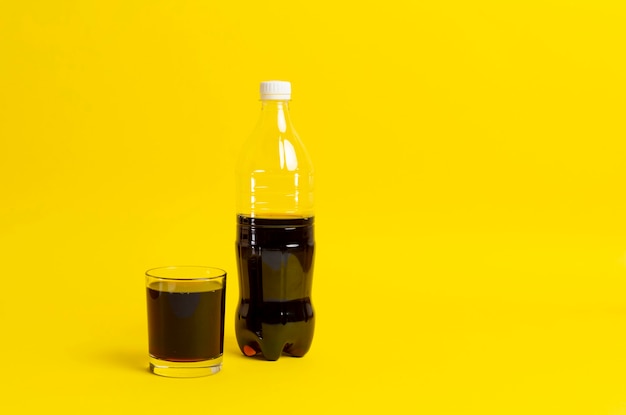 Una limonada negra vertida en el vaso, botella de refresco aislado sobre fondo de color