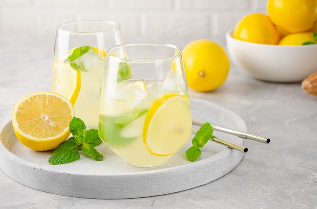 Limonada tradicional con limón, menta y hielo en un vaso con pajita de metal sobre un fondo de hormigón gris.