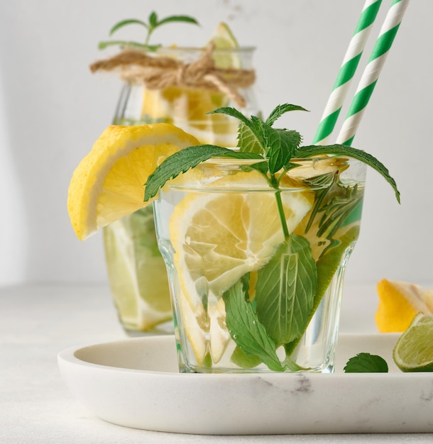 Limonada en un vaso transparente con ramitas de romero de lima limón y hojas de menta sobre un fondo blanco