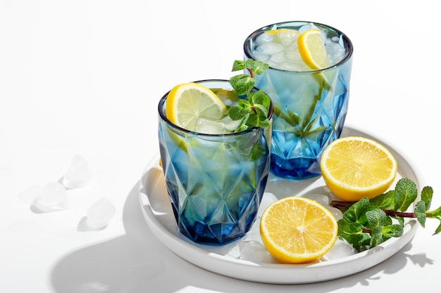 Limonada de verano con menta y hielo en vasos azules sobre una mesa blanca en un plato