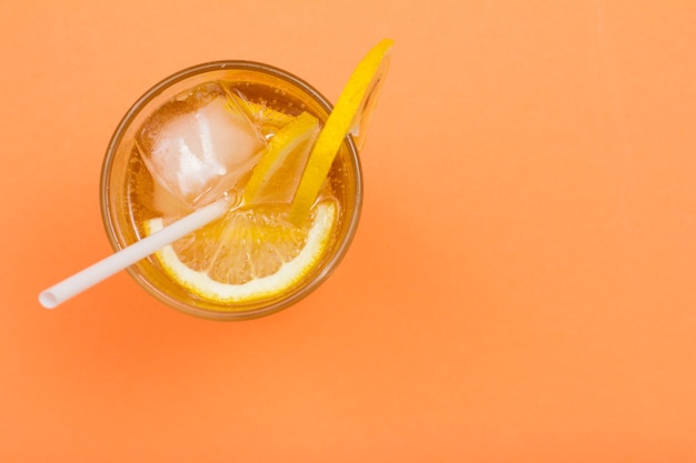 Limonada de verano refrescante fría con hielo y rodajas de limón en un vaso alto sobre fondo de color melocotón con espacio de copia. Vista superior