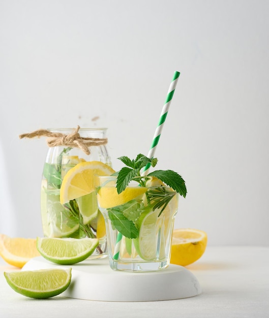 Limonade in einem durchsichtigen Glas mit Zitronen-Lime-Rosmarin-Zweigen und Minzblättern auf weißem Hintergrund