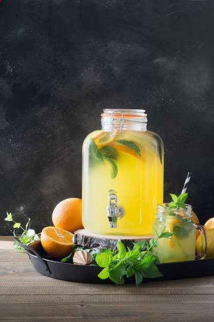 Limonade mit Orange, Zitrone und Minze im Weckglas auf schwarzem und hölzernem Brett.