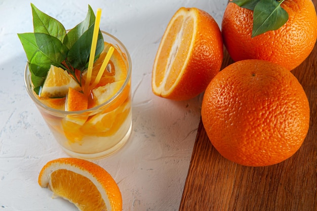 Limonade mit Orangen mit Orangenscheiben und ganzen Orangen auf weißem Hintergrund und einem jungfräulichen Brett Sommerstimmung und morgendliches Frühstück