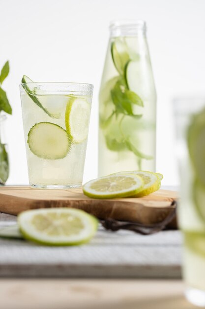 Limonadenflasche und ein Glas serviert mit Zitronen- und Gurkenscheiben auf hellem Hintergrund, Kopierraum