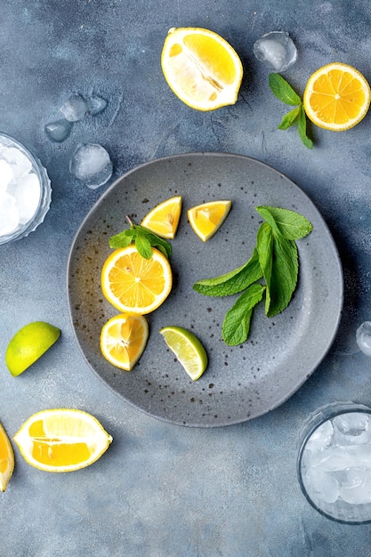 Limonadenzubereitungsglas mit Eiswürfeln frischen Zutaten Zitrone und Minze auf grauer Keramikplatte