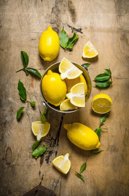 Limones frescos en un cubo de hojas sobre una mesa de madera. Vista superior