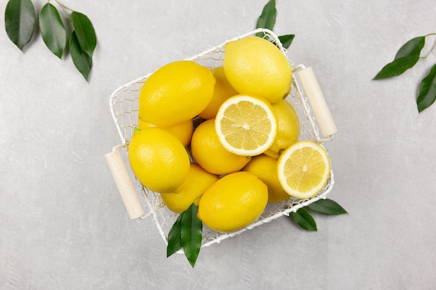 Limones frescos con hojas en una canasta blanca sobre superficie de hormigón gris claro