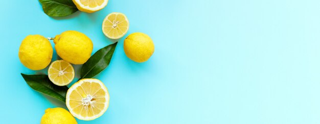 Limones maduros jugosos y hojas verdes sobre fondo azul brillante. Fruta de limón, concepto mínimo de cítricos, vitamina C. Fondo minimalista de comida creativa de verano. Endecha plana, vista superior, espacio de copia, banner