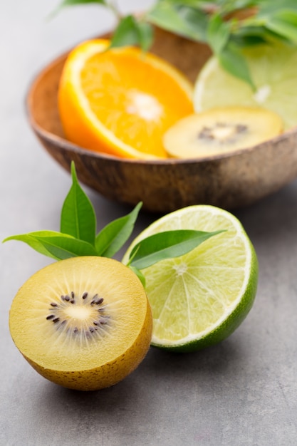 Limones mixtos de frutas cítricas, naranja, kiwi, limas sobre una superficie gris.