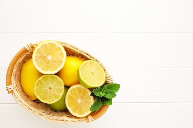 Limones orgánicos y limas en una cesta en la pared de madera blanca con espacio de copia