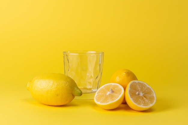 Limones y vaso de vidrio vacío sobre un fondo amarillo