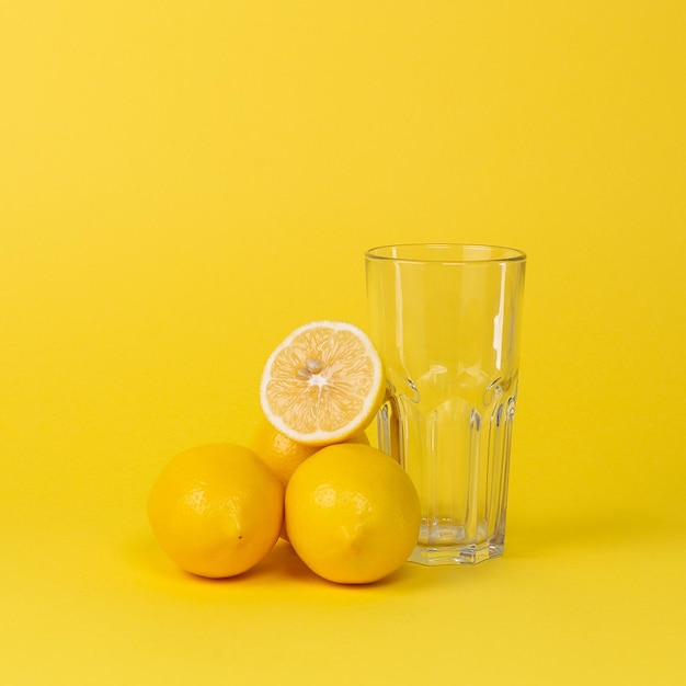 Foto limones y vaso de vidrio vacío sobre un fondo amarillo