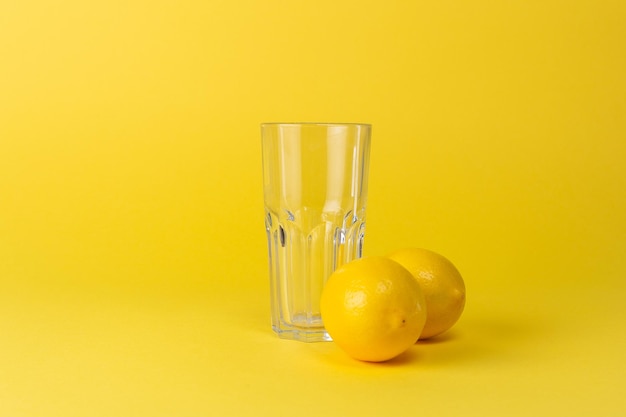 Limones y vaso de vidrio vacío sobre un fondo amarillo