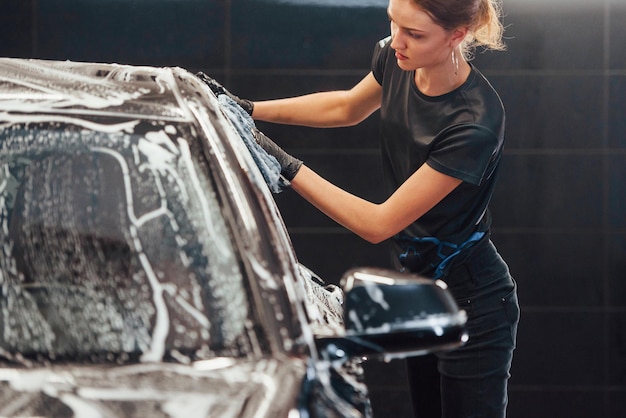 Limpa o veículo que está em sabão branco O automóvel preto moderno é limpo pela mulher dentro da estação de lavagem de carros