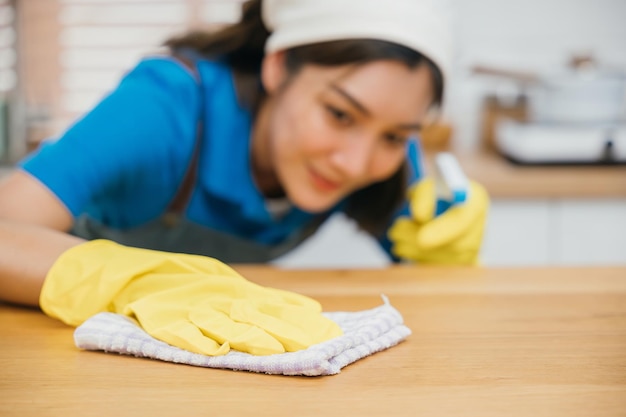 Limpador profissional asiático com luvas amarelas limpa o balcão da cozinha usando spray líquido O serviço de limpeza destaca a limpeza e a higiene da casa Limpeza, desinfecção, cuidados domiciliares, empregada doméstica