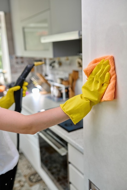 Limpando a geladeira com um pano de poeira e graxa, a garota faz a limpeza na cozinha pela geladeira limpando com um gerador de vapor