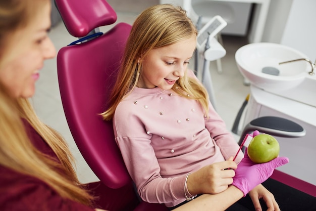 Limpando maçã com dente Menina visitando dentista na clínica Concepção de estomatologia