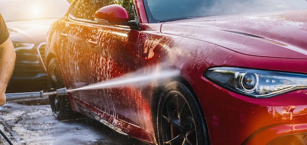 Limpando o carro vermelho usando água de alta pressão em uma lavagem de carro