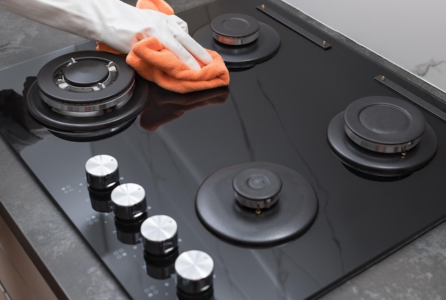 Foto limpando o fogão a gás mão da pessoa em uma luva de borracha, polindo o vidro com um pano de microfibra