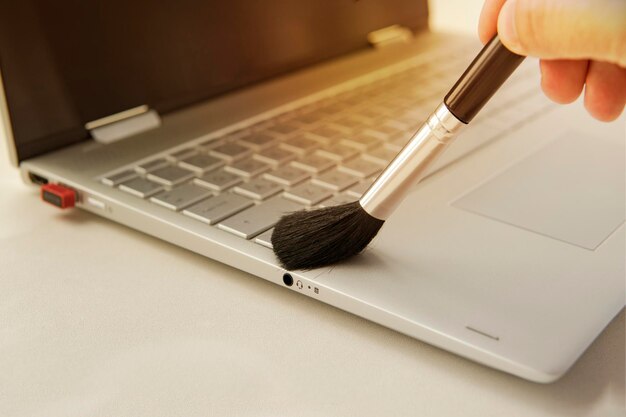 Limpando o teclado e cuidando do computador Mão masculina com uma escova para remover a poeira do teclado limpando o teclado do transformador ultrabook cinza moderno com uma escova preta da poeira