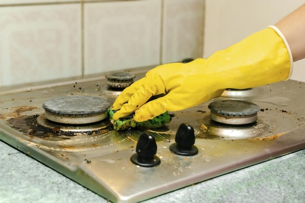 Limpar o fogão a gás sujo das sobras de comida gordurosa deposita a mão da mulher na luva protetora com pano de esponja e detergente lavando o conceito de serviço de limpeza doméstica do fogão de cozinha