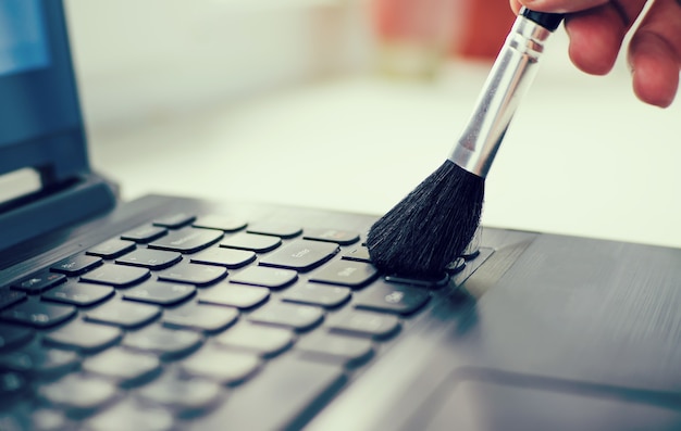 Foto limpar teclado e cuidar do computador. mão masculina com uma escova para remover a poeira do teclado