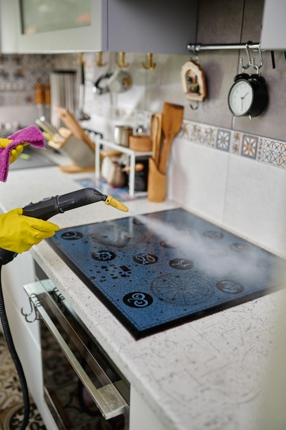 Limpar um fogão elétrico elegante com um gerador de vapor O vapor limpa a superfície da sujeira Cozinha branca Limpeza no apartamento