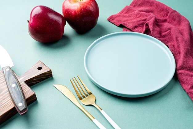 Limpe a placa verde de maquete de prato vazio com talheres e maçãs vermelhas e guardanapo na mesa verde