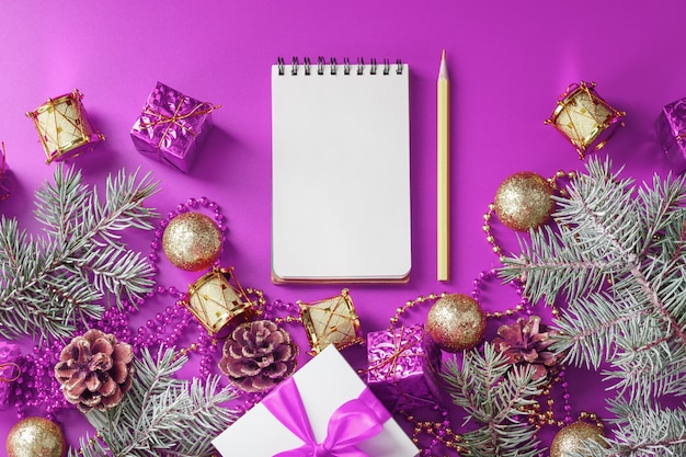 Limpe o bloco de notas branco com lápis ao redor das decorações de natal na mesa roxa. planejamento, lista de desejos e resolução 2021. a visão do topo