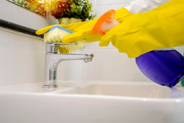 Limpe o conceito de torneira do banheiro, use luvas de borracha amarela, pulverize o detergente e esfregue com uma esponja Louça sanitária branca