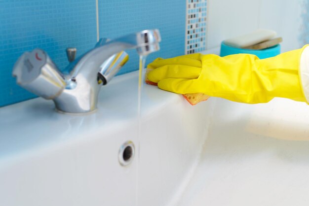 Limpeza da pia do banheiro e torneira com detergente em luvas de borracha amarela com esponja laranja