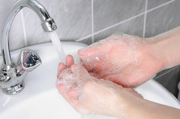 Limpeza das mãos de bactérias e vírus da sujeira com água da torneira no banheiro para proteger contra gripe e doenças