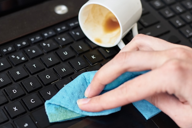 Foto limpeza das mãos de café derramado no teclado do laptop