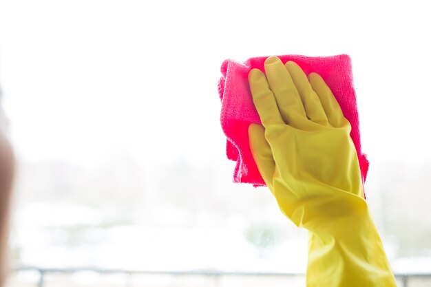 Limpeza de janelas com pano especial e detergente em luvas amarelas em casa