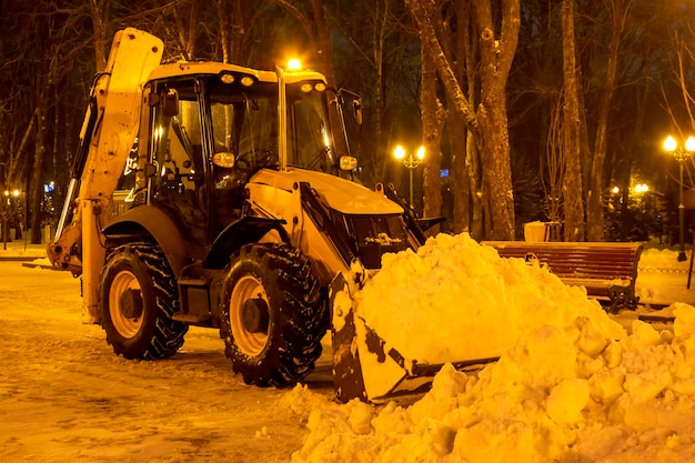 Limpeza de neve no parque no inverno com um trator à noite