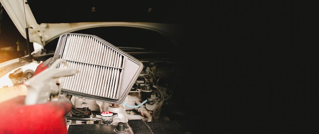 Limpeza do filtro de ar do carro com pistola de ar pela mão do mecânico automático no espaço de cópia horizontal da faixa horizontal da garagem de reparação automóvel em fundo preto