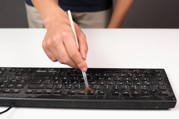 Limpeza do teclado do computador no escritório com luva protetora de borracha e uma escova de trabalho doméstico empoeirado