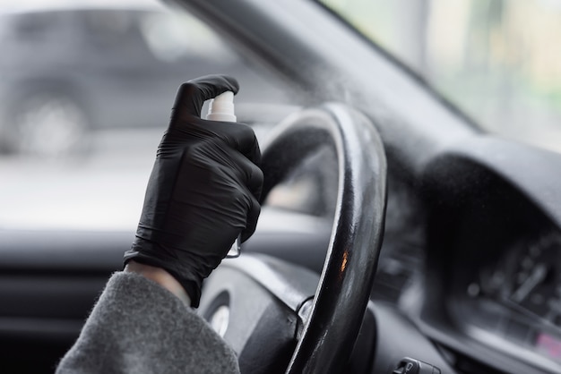 Limpeza interior do carro e pulverização com líquido de desinfecção. mãos na luva protetora de borracha que desinfetam o veículo dentro para proteção contra doenças virais