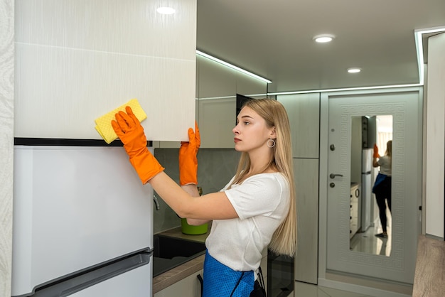 Limpeza muito jovem empregada doméstica com spray e esponja no trabalho doméstico ktchen