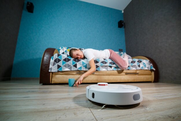 Limpeza simples e fácil com tecnologia moderna para o uso doméstico. menina bebe chá e descansa enquanto o aspirador faz a limpeza da casa