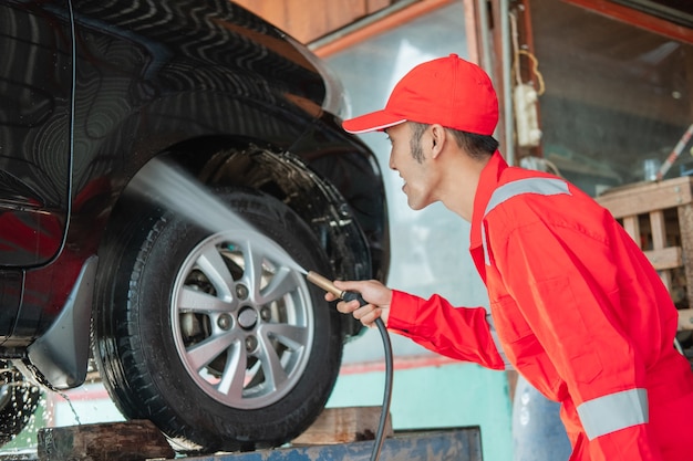 Limpiador de automóviles masculino con uniforme rojo y sombrero está rociando aire tan suelto como un automóvil en el salón del automóvil