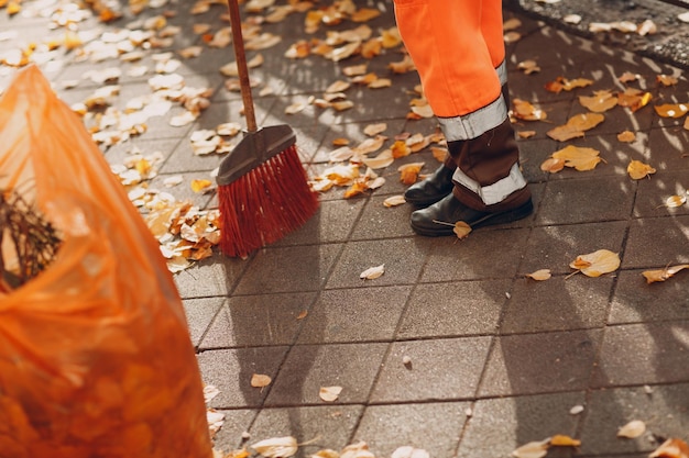 Limpiador de conserje barriendo hojas de otoño en la calle