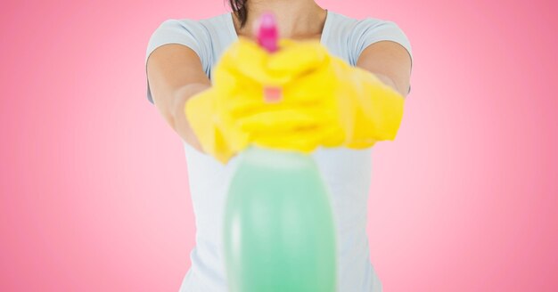 Limpiador femenino sosteniendo una botella de spray de limpieza contra el fondo de color rosa