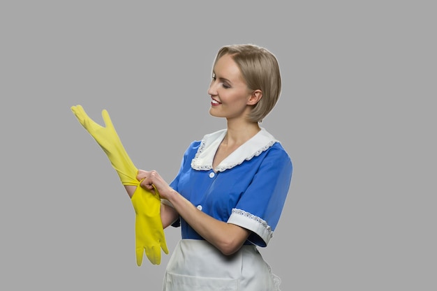 Foto limpiador de mujer alegre se pone guantes. la criada sexy sonriente en uniforme azul está lista para trabajar.