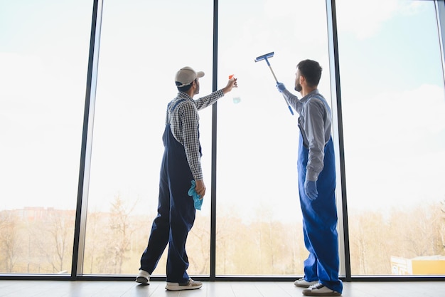 Limpiadores profesionales multiétnicos en uniforme lavando grandes ventanas en la oficina