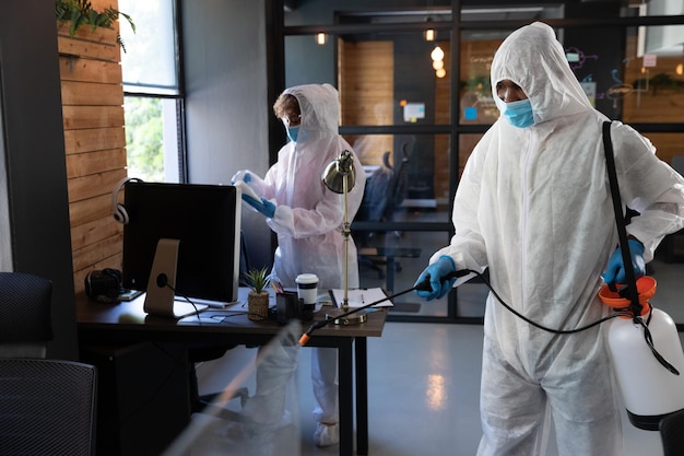 Limpiadores de raza mixta con trajes protectores en una oficina. desinfectar la oficina. higiene en el lugar de trabajo durante la pandemia del coronavirus covid 19.