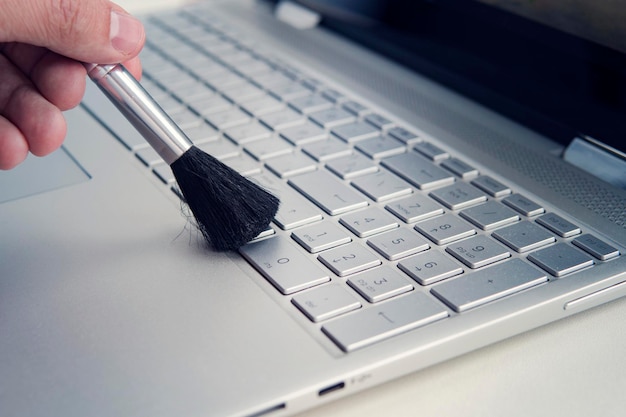 Limpiando y cuidando la computadora limpiando el teclado del moderno transformador ultrabook gris con un cepillo negro del polvo