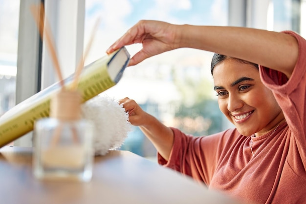 Limpiando el hogar y la mujer desempolvando el estante de libros para eliminar el polvo y la suciedad Servicio de limpieza de limpieza de primavera y feliz limpiadora o ama de llaves con plumero para tareas de muebles e higiene