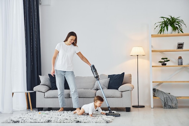 Limpiando el piso usando una aspiradora La madre con su pequeña hija está adentro en casa juntos